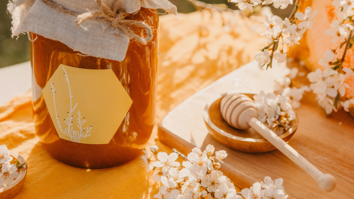 un pot de miel artisanal posé sur une table entouré de fleurs blanches